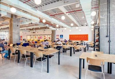 Large open-plan workspace with multiple wooden desks and industrial ceiling details.