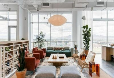 Sunlit communal lounge with colorful seating, area rug, and mountain views through floor-to-ceiling windows.