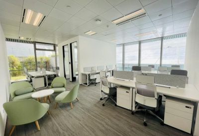 Modern office lounge featuring light green armchairs and a small coffee table near workstations.