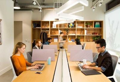 Open-plan office with long wooden desks and ergonomic chairs.