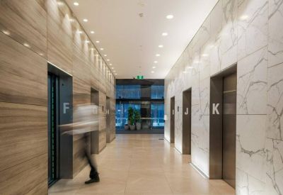 Bright elevator bank with wood and marble walls and marked lift doors.