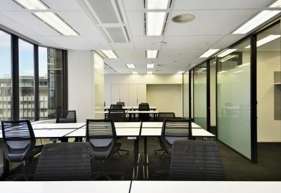 Bright open-plan workspace with banks of white desks and black mesh chairs.