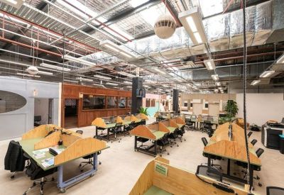 Spacious open-plan workspace with multiple wooden desks and industrial exposed ceiling.