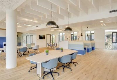 Open-plan coworking space featuring shared tables with blue chairs and private booth seating.