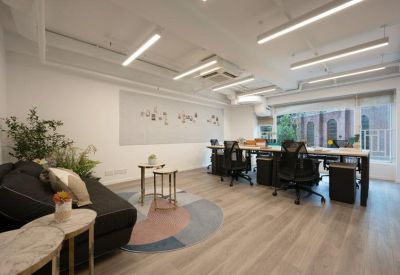 Open-plan office space with ergonomic black chairs, long desks, and a decorative area rug.