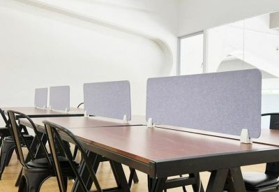 Coworking office space featuring long wooden desks with grey privacy dividers and black chairs.