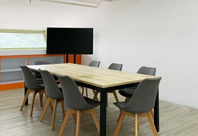 Modern meeting room with a light wood table, grey chairs, and a large monitor display.