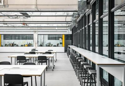 Open-plan workspace featuring long white tables with black chairs and window-side bar seating.