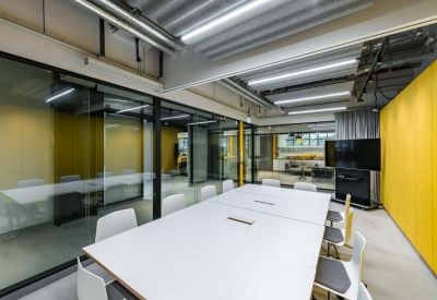 Bright glass-walled meeting room with a large white table and yellow feature wall.