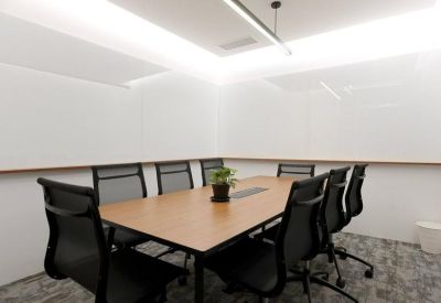 Bright meeting room with a large wooden table, black mesh chairs, and whiteboard walls.