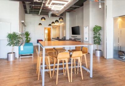 Communal breakout area with high wooden tables, stools, and indoor plants.