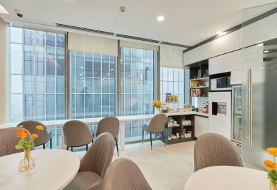 Bright dining area with round tables and a kitchen station by large windows.