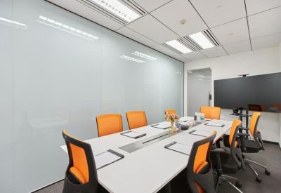 Modern conference room with orange chairs around a white table and a wall-mounted screen.