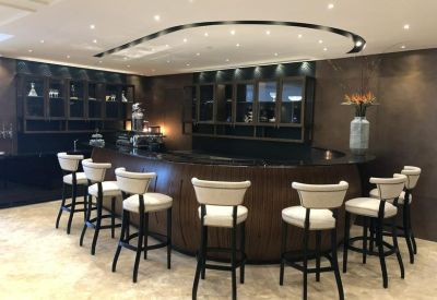 Sleek dark wood bar area with circular ceiling light and elegant white bar stools.
