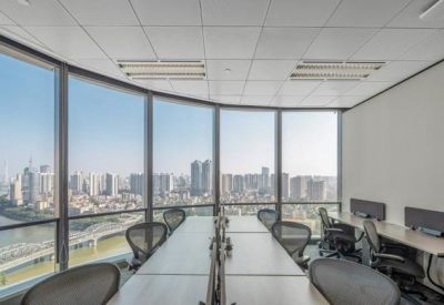 Bright open-plan office with desks facing floor-to-ceiling windows with city views.