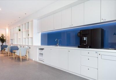 Modern office kitchen featuring a blue glass backsplash and integrated coffee station.
