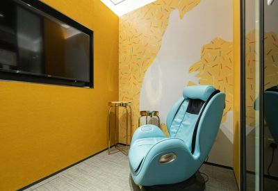 Relaxation room with a light blue massage chair and vibrant yellow feature wall.