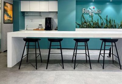 Communal break area with a long white counter and four black bar stools against a teal wall.