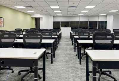 Large open-plan training room or office with rows of white desks and black mesh chairs.
