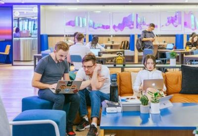 People working in a vibrant communal lounge with blue ottomans and an orange sofa.