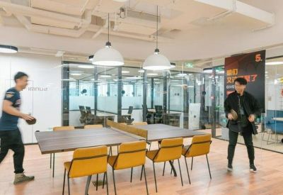 Spacious recreational area with a ping pong table and yellow seating in front of glass offices.