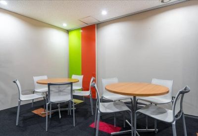 Open-plan coworking space with large wooden tables and city views through wide windows.
