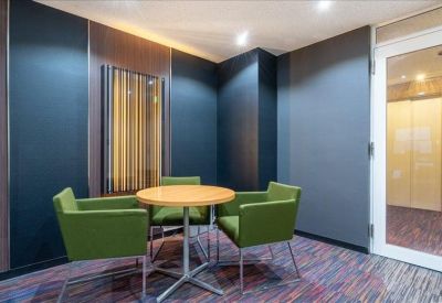 Small meeting room featuring a wooden table and four black chairs in a minimalist white space.
