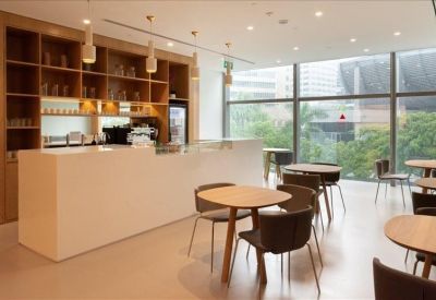 Modern office café and breakout area with a white counter and wooden tables.