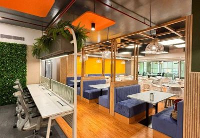 Coworking area with long white desks, blue booths, and vibrant orange ceiling panels.