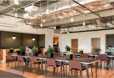 Bright open-plan office with long wooden tables and rows of brown chairs.