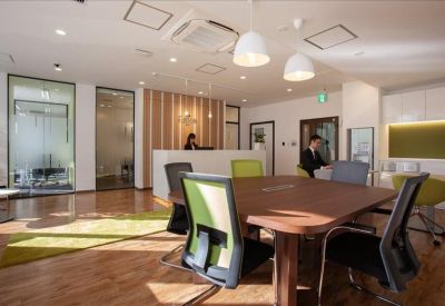 Bright reception area with a white front desk, green chairs, and wooden flooring.