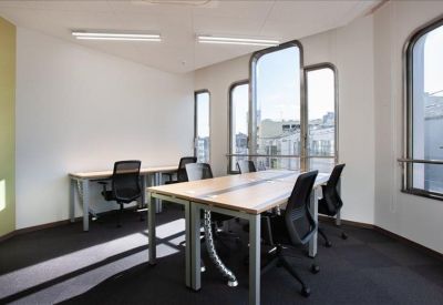 Shared workspace with wooden desks and black mesh chairs near unique arched windows.