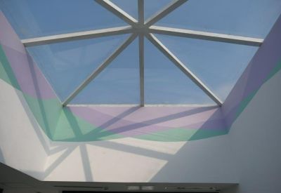 Internal view of a geometric glass skylight casting artistic shadows on colorful painted walls.