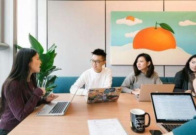 Team meeting around a wooden table with laptops and colourful wall art.