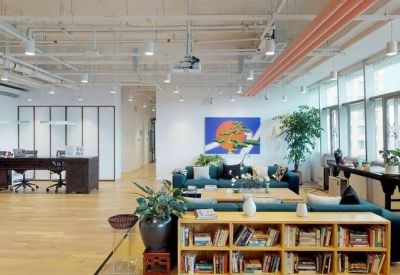 Bright reception area featuring a low wooden bookshelf, seating area, and wide-plank wood floors.