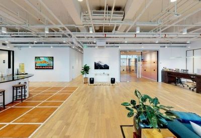 Wide open-plan office corridor showing a workspace area with a dark desk and glass partitions.