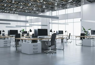 Industrial style open-plan office with rows of white desks and an exposed ceiling.