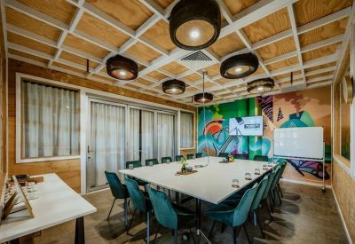 Professional meeting room with a large square table, teal chairs, and a creative grid ceiling.