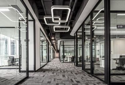 Long office corridor with glass partitions and recessed square ceiling lights.