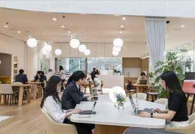 Spacious coworking area with round pendant lights and people working at large communal tables.