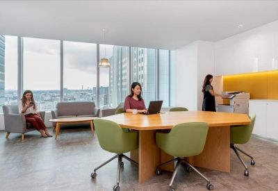 Collaborative workspace with a hexagonal wood table, green chairs, and large windows with city views.