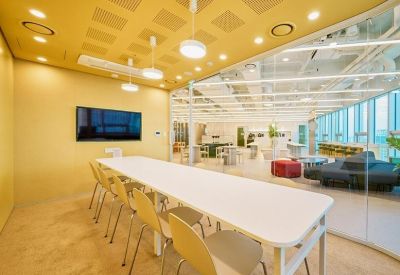 Meeting room with a long white table, yellow walls, and a glass partition showing a workspace.