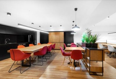 Modern communal break area with vibrant red chairs and a long wooden dining table.