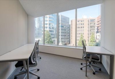 Bright open-plan office featuring long white desks and ergonomic grey chairs near windows.