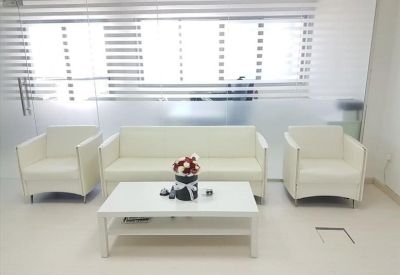 Bright reception lounge featuring a white sofa, armchairs, and a matching coffee table.