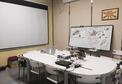 Bright meeting room with a large white conference table, projection screen, and whiteboards.