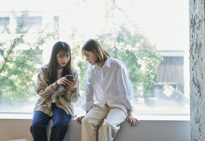 Two colleagues sitting by a large window, collaborating and looking at a smartphone.
