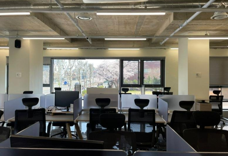 Spacious open-plan workspace at Dowon Hall with rows of desks and large windows overlooking trees.