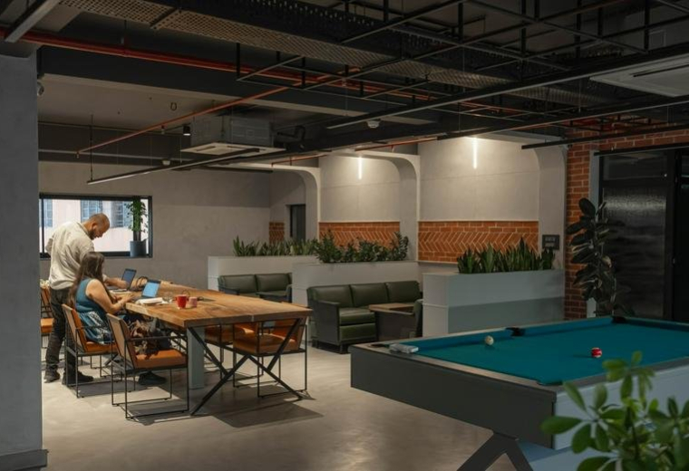 Spacious breakout area with a pool table, wooden communal desk, and green leather sofas.
