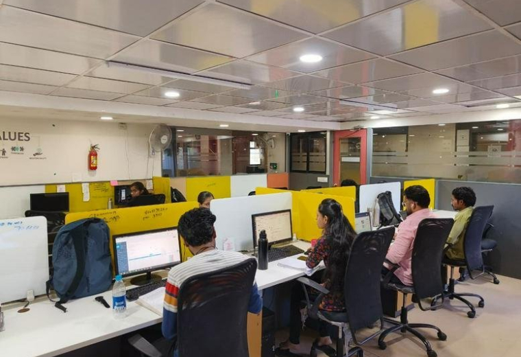 Shared workspace with employees at their desks under bright recessed lighting.